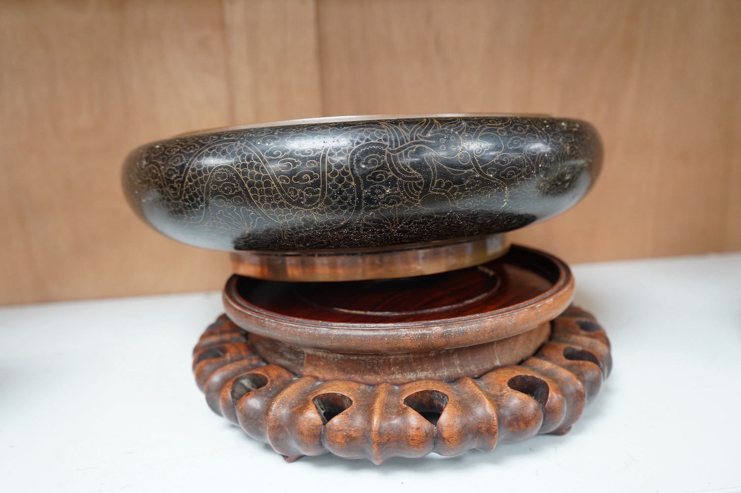 A Chinese black ground cloisonné enamel ‘dragon’ bowl on a carved hardwood stand, 14.5cm high. Condition - fair